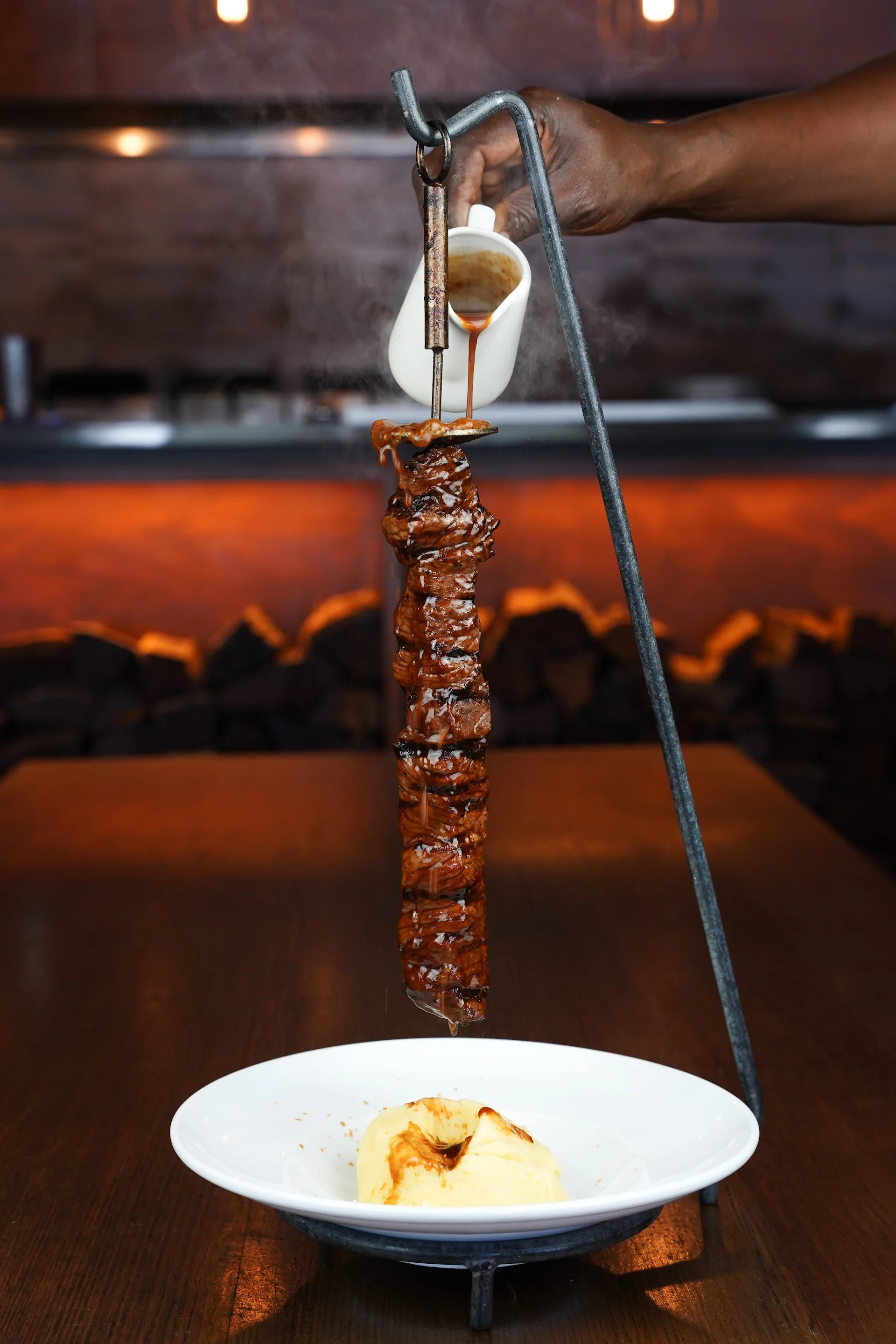 Chef pouring jus over a hanging beef skewer at Waterbar & Grill Steakhouse, Cairns