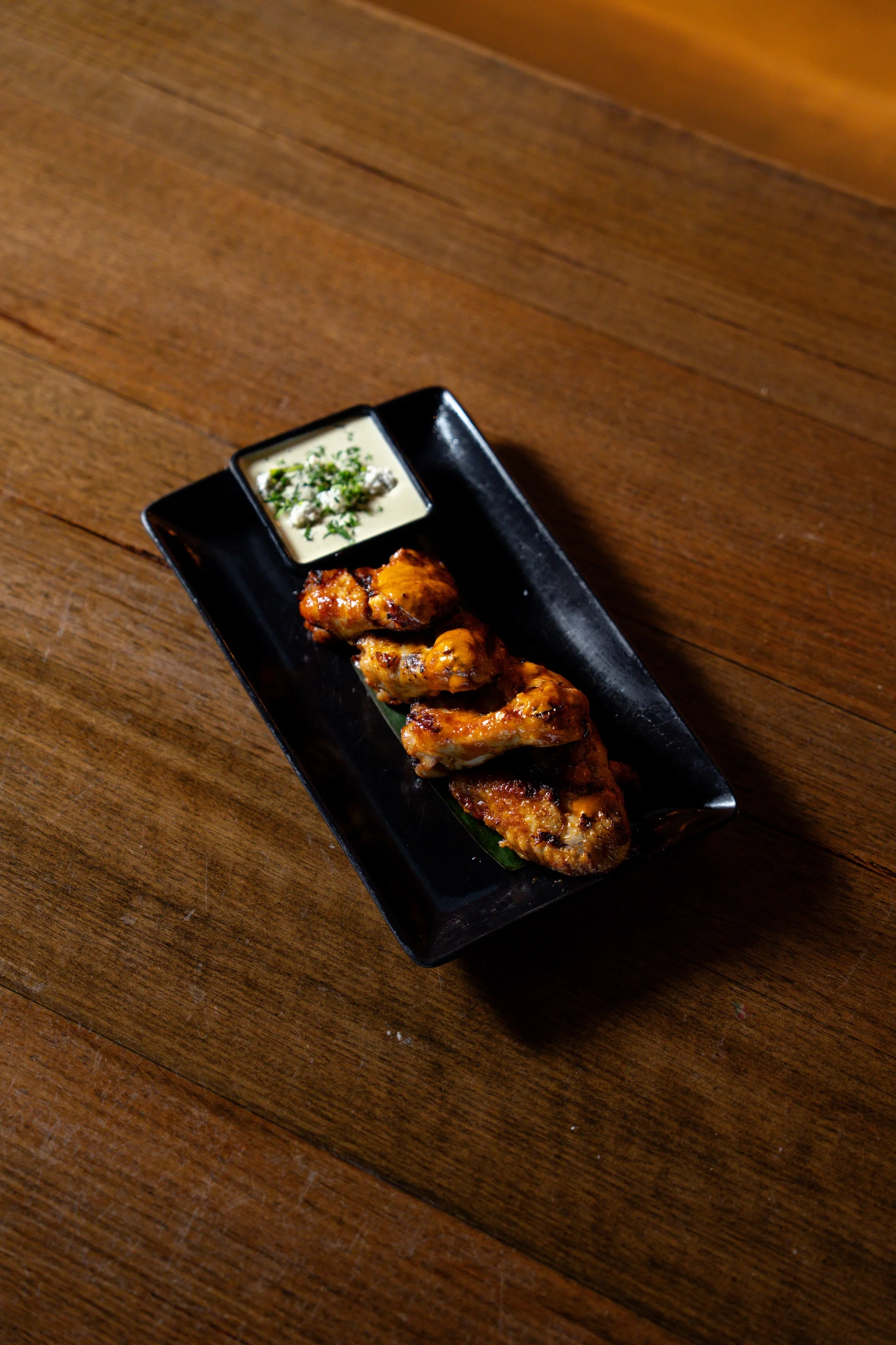 Grilled chicken wings with aioli on a black plate at Waterbar & Grill Steakhouse, Cairns